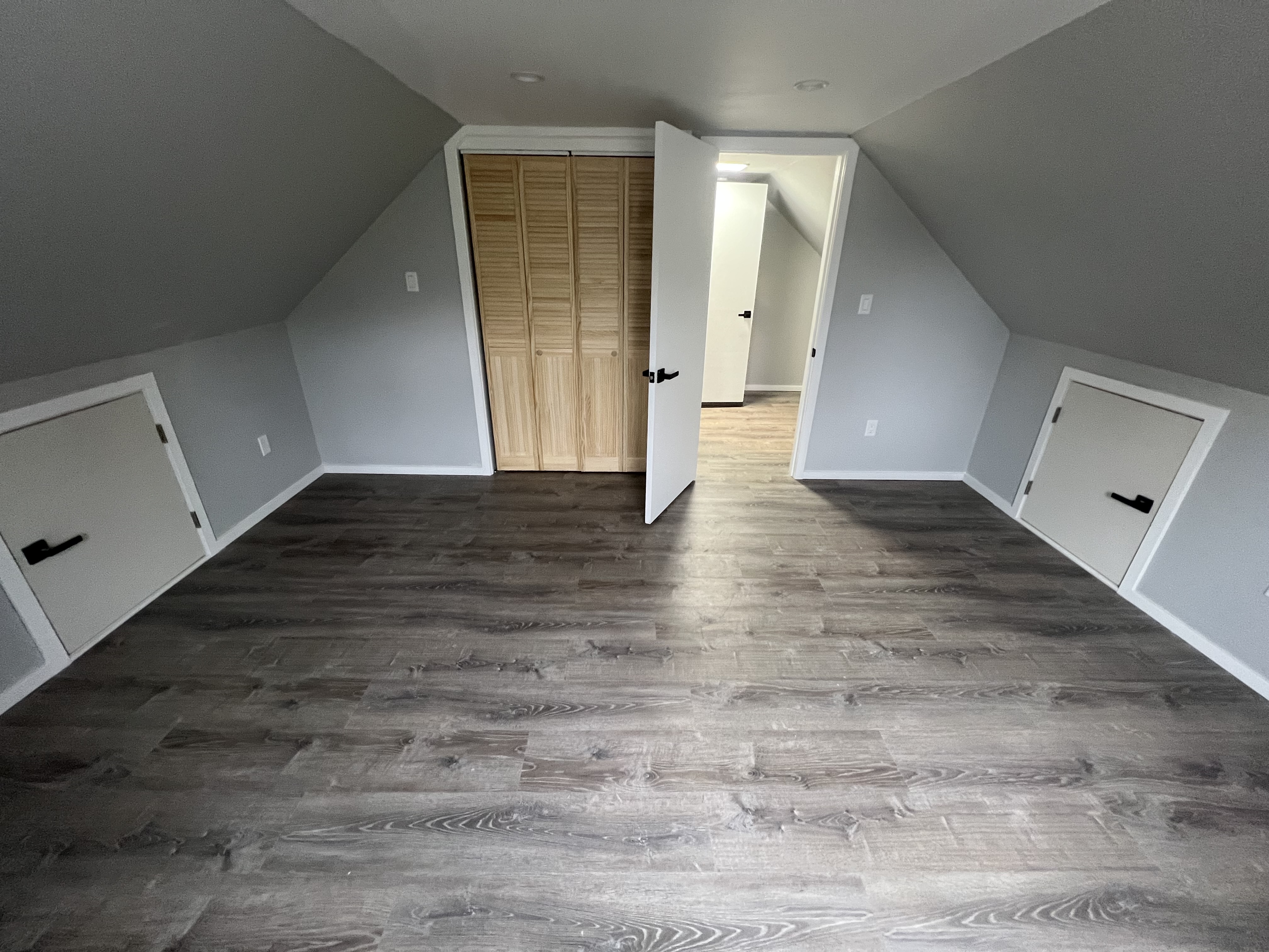 Finished attic room with gray flooring, closet doors, and sloped walls.