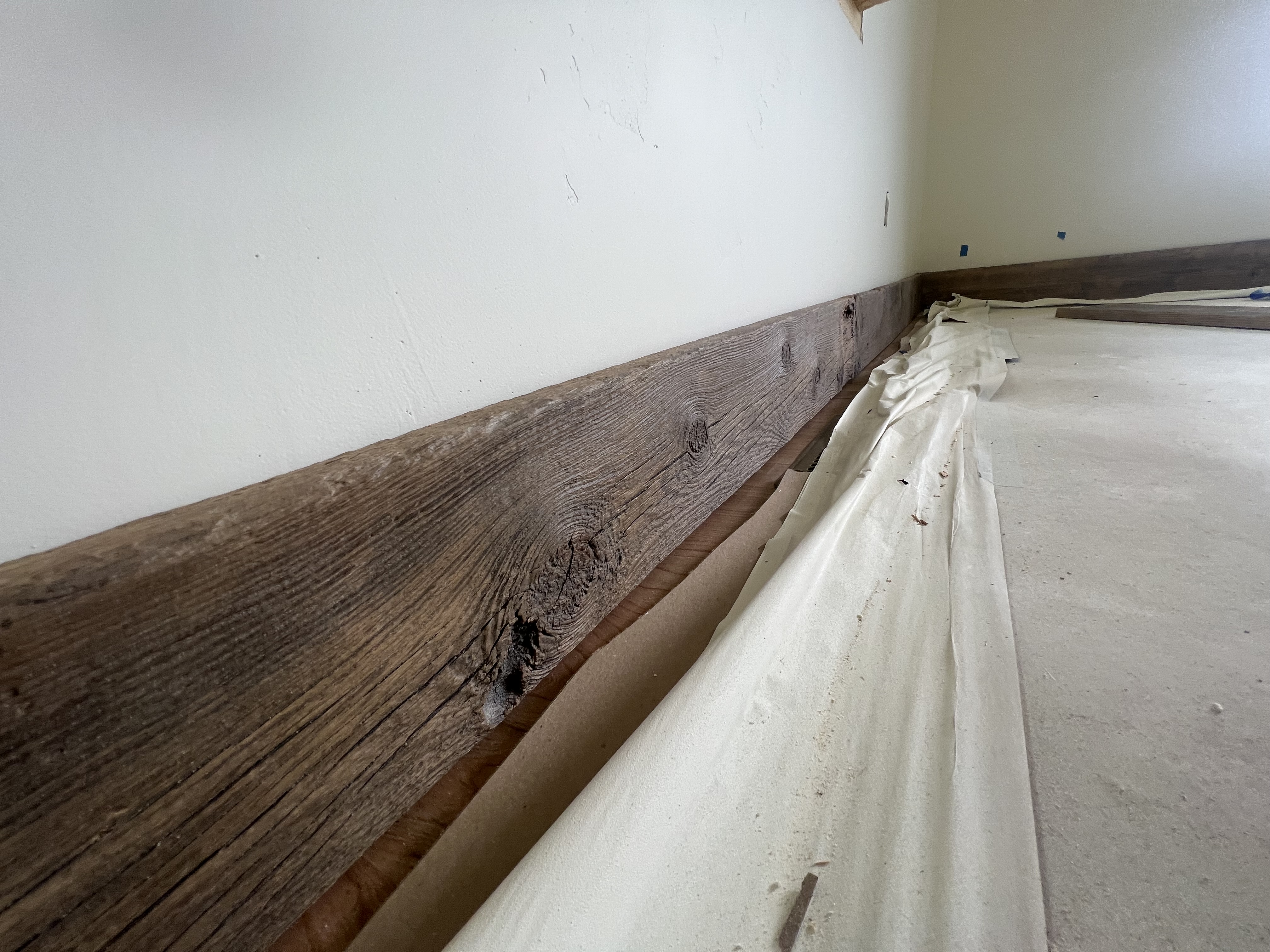 Rustic wood baseboard trim being installed along a wall.
